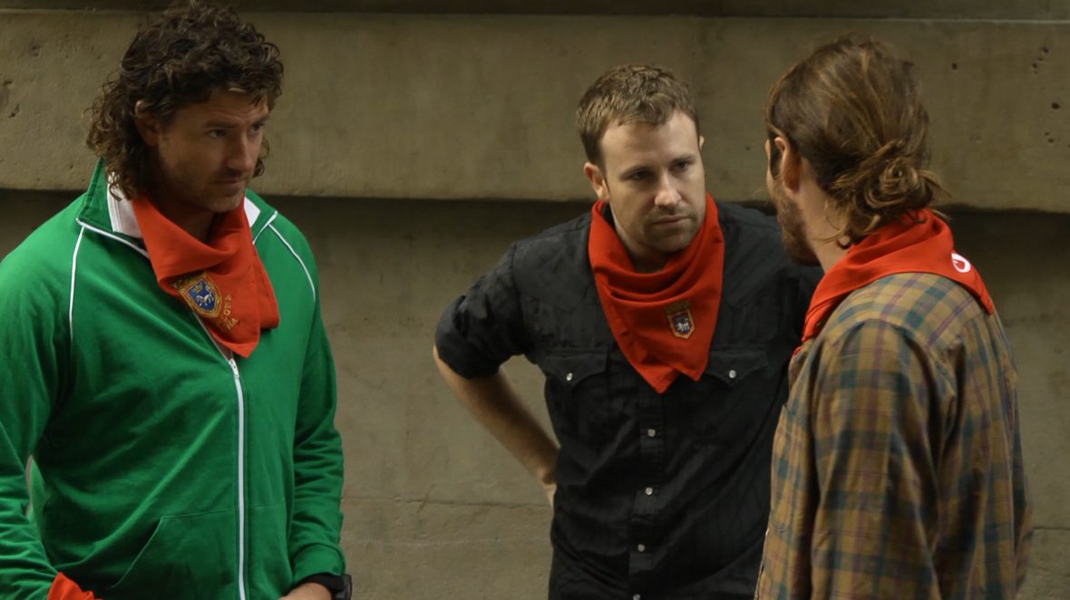 Three runners wearing red pañuelos talk in a Pamplona street in the documentary Chasing Red